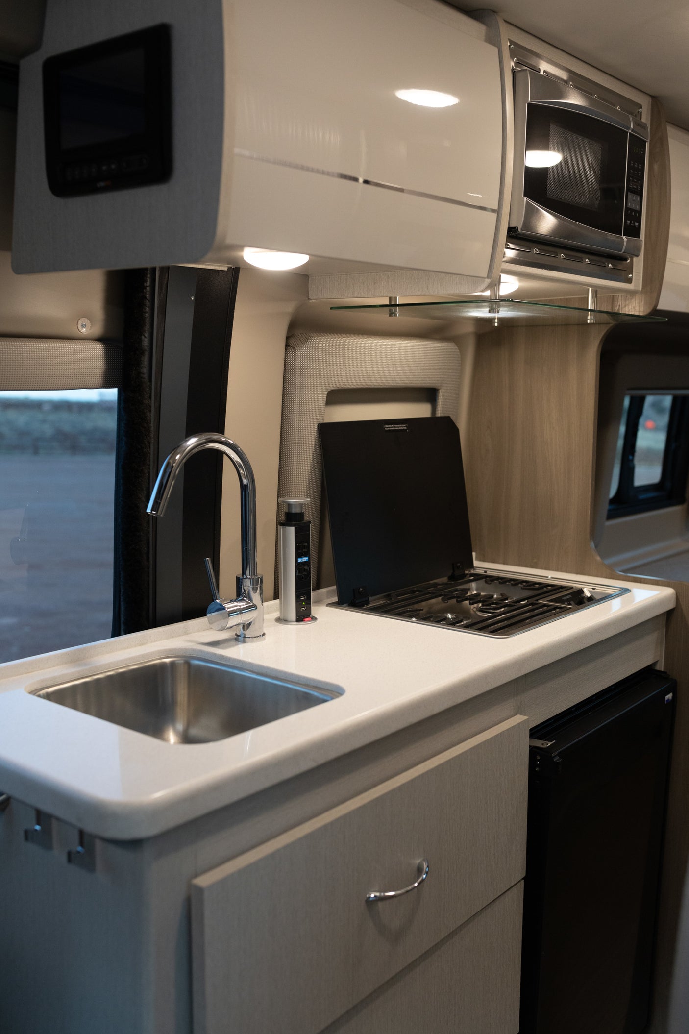 Explore this modern RV rental kitchen. Features a stainless steel sink, covered stove, microwave, and sleek cabinetry for travel.