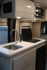 Explore this modern RV rental kitchen. Features a stainless steel sink, covered stove, microwave, and sleek cabinetry for travel.