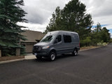Gray Mercedes Sprinter van, an ideal RV rental, parked on an asphalt road in a residential area under cloudy skies.