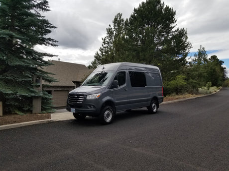 Gray Mercedes Sprinter van, an ideal RV rental, parked on an asphalt road in a residential area under cloudy skies.
