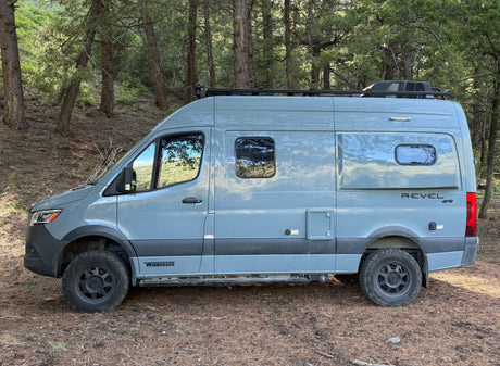 Grey Winnebago Revel 4x4 camper van, an ideal RV rental, parked amidst a serene forest.