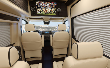 Luxurious rv rental interior: cream leather seats, a large TV playing football, and pleated window blinds for comfort.