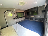 RV rental: Compact, comfortable interior with a bed, TV, and essentials for your next adventure.