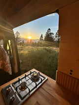 Experience epic sunrises from your RV rental! This camper van's kitchen stove offers mountain & forest views.