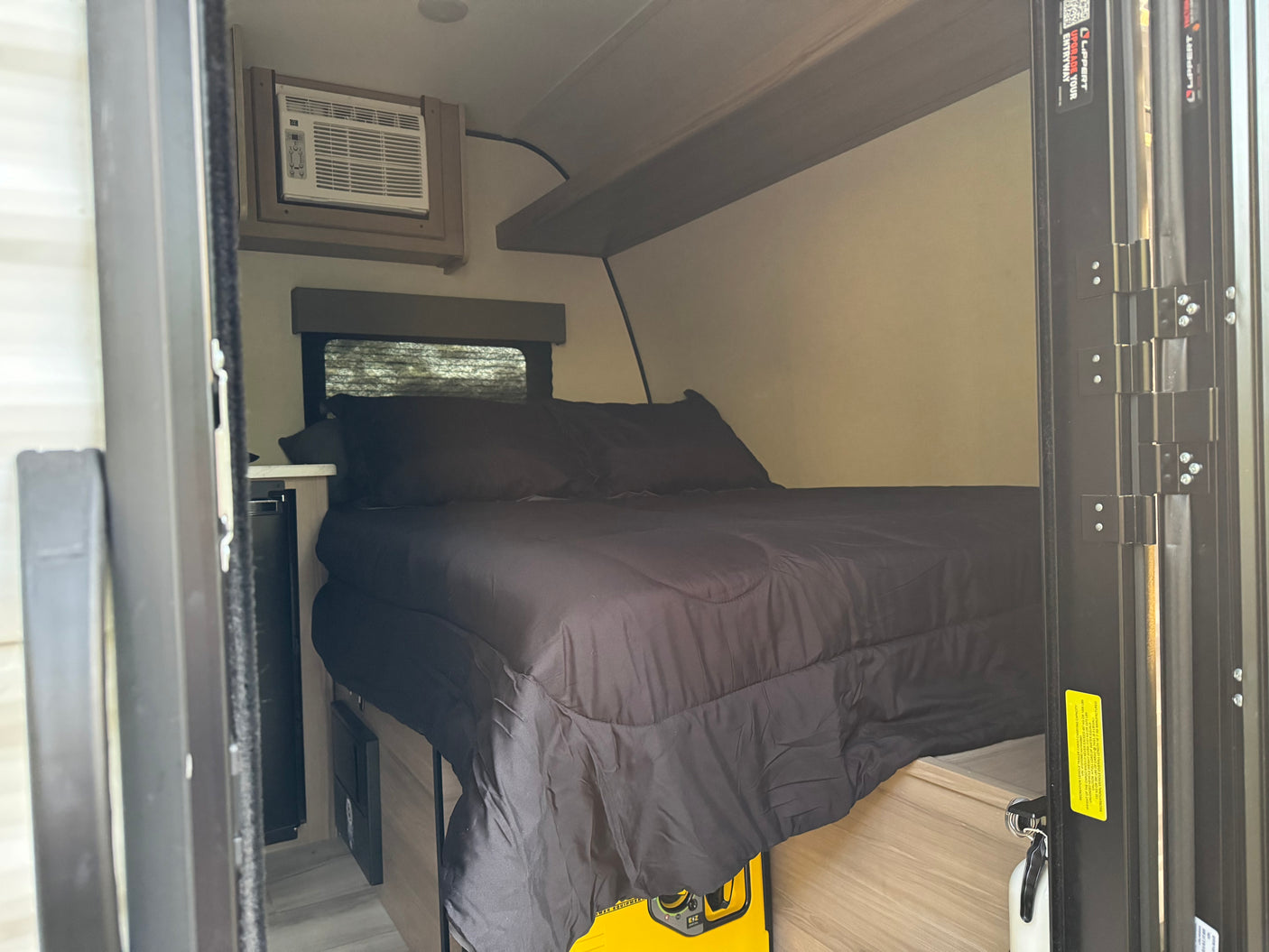 Cozy RV rental bedroom with black bedding, AC unit, window, and portable power. Compact and comfortable for travel.