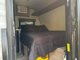 Cozy RV rental bedroom with black bedding, AC unit, window, and portable power. Compact and comfortable for travel.