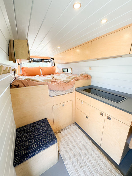 Cozy rv rental interior showcasing a raised bed, kitchenette, and light wood cabinetry for comfortable travel.