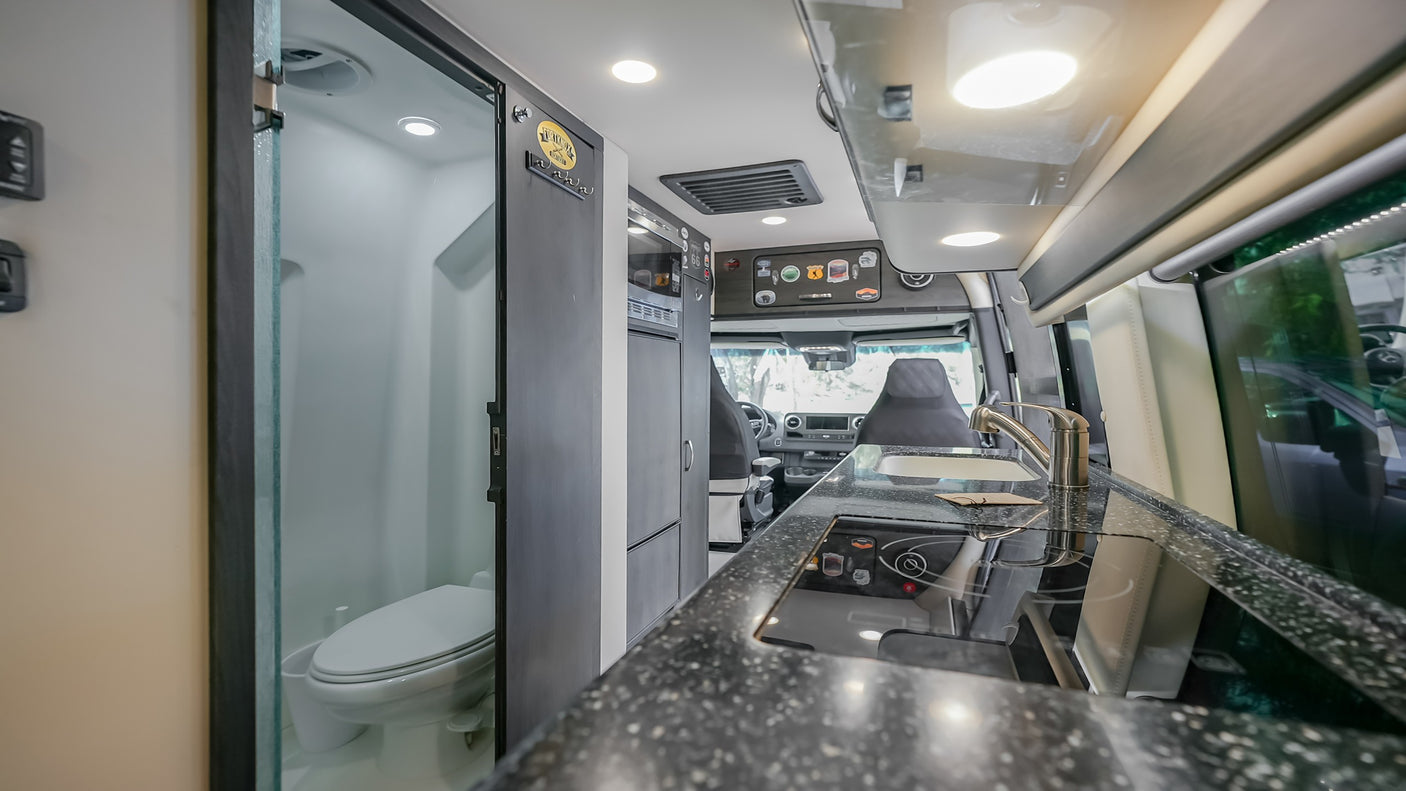This modern RV rental camper van features a full kitchen with sink, induction cooktop, and a compact bathroom.