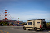 Tan RV rental van parked near the Golden Gate Bridge, San Francisco. Features a roof rack and ladder.