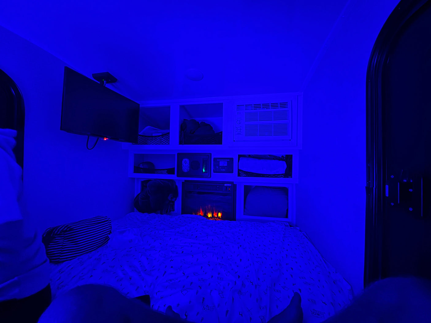 Cozy blue-lit RV rental interior with bed, TV, AC, and electric fireplace. Enjoy relaxing amenities in this compact space.