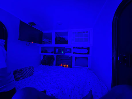 Cozy blue-lit RV rental interior with bed, TV, AC, and electric fireplace. Enjoy relaxing amenities in this compact space.