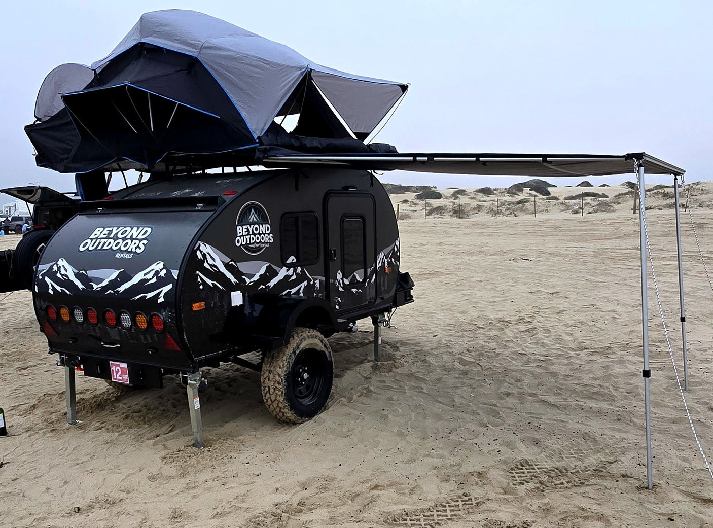 Beyond Outdoors off-road rv rental trailer with rooftop tent & awning setup on sand for adventure camping.