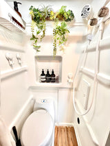 Compact RV rental bathroom features a modern toilet, shower, Aesop toiletries, and decorative plants, optimizing small space comfort.