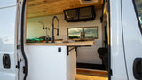 This RV rental features a modern kitchen with a black faucet, wood counters, and a scenic window view of a city skyline.