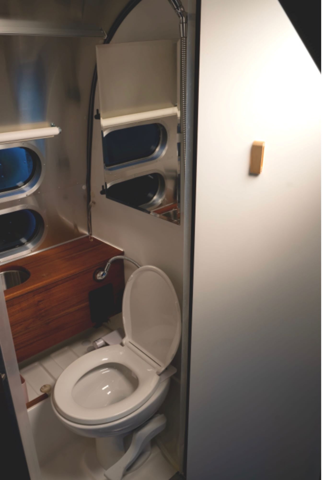 Sleek aluminum interior of an RV rental bathroom, featuring a toilet, wooden vanity, and shower. Compact design for travel.