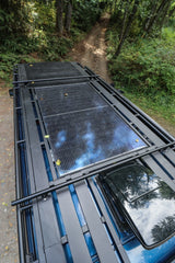 Overhead view of an RV rental with solar panels, roof rack, and skylight, on a wooded dirt road. Ready for adventure.