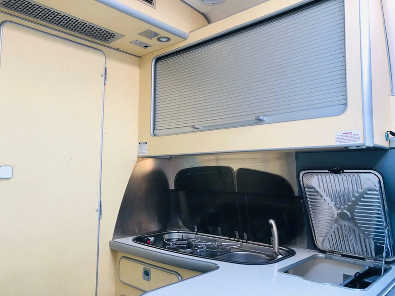 RV rental interior: a compact kitchen area with a two-burner stove, sink, and a louvered cabinet for storage. — photo 14