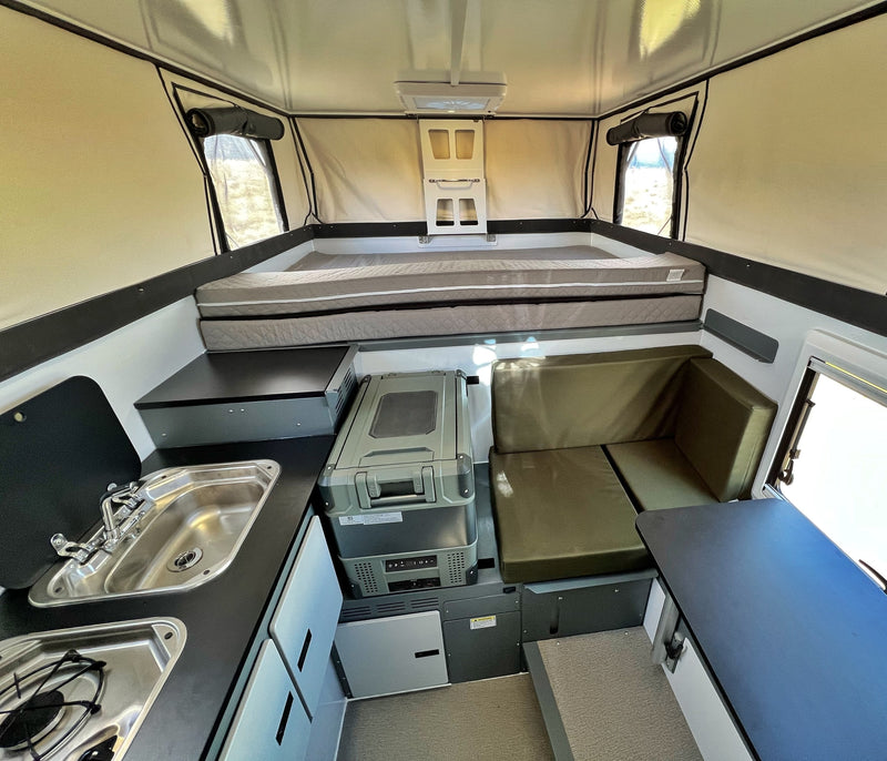 Spacious rv rental interior: pop-up camper with comfortable bed, kitchen (sink/stove), portable fridge, and dinette seating. — photo 9
