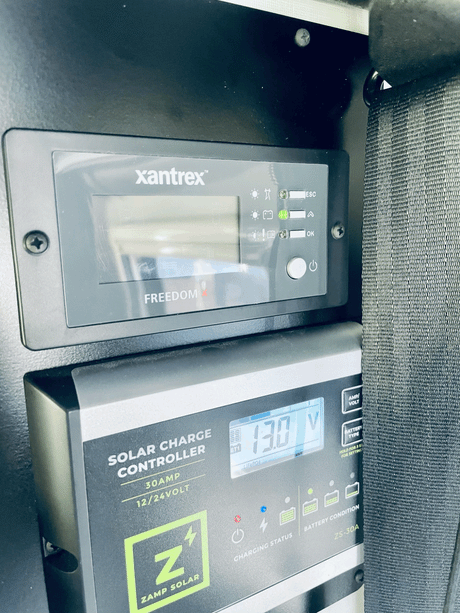 RV rental: A Zamp Solar charge controller displays 13.0V below a Xantrex power monitor, managing battery charging.