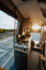 RV rental camper kitchen with stove, sink, and fridge, bathed in golden sunset light. Perfect for mobile adventures.