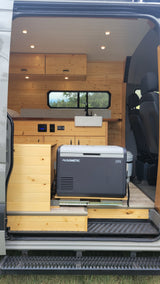 RV rental: Cozy camper van interior with wood walls, kitchen sink, Dometic fridge, and portable toilet, perfect for mobile adventures.