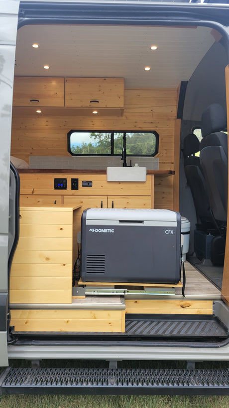 RV rental: Cozy camper van interior with wood walls, kitchen sink, Dometic fridge, and portable toilet, perfect for mobile adventures.