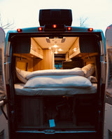 Open rear view of a cozy RV rental, revealing a comfortable bed, overhead cabinets, and under-bed storage for travel.