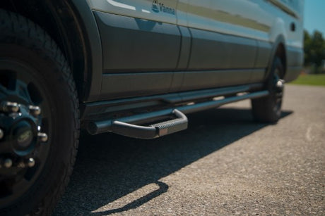 Lower side of an RV rental van with rugged black wheels and an off-road side step, parked on asphalt.