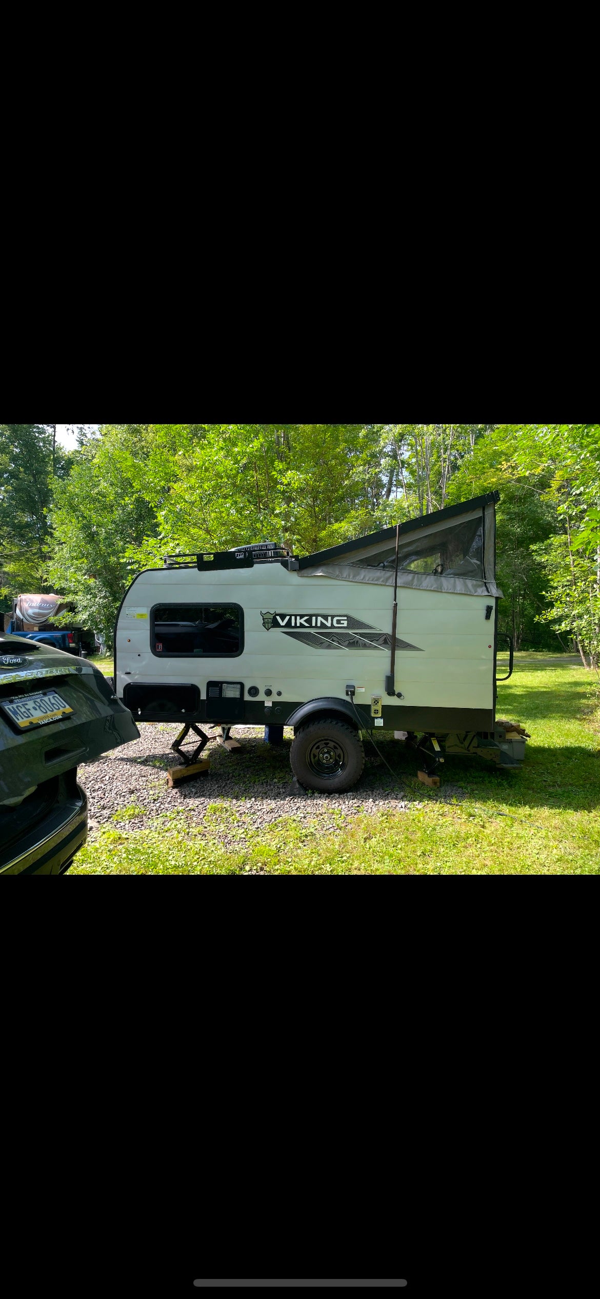 Light grey Viking pop-up camper, ready for an rv rental adventure in a green, wooded campsite.