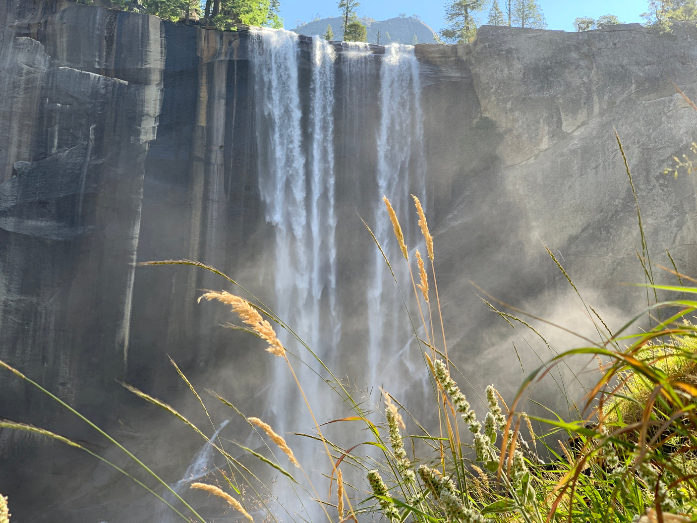 Powerful waterfall cascading, creating heavy mist. Sunlit golden grasses frame the foreground. Ideal for an RV rental adventure.