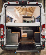 Discover a modern camper van interior with an elevated bed, versatile storage, and a pull-out ramp, ideal for your next RV rental.