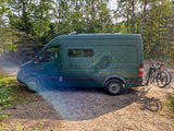 Green Sprinter camper van with bikes parked on a dirt road, perfect for an RV rental adventure in the forest.
