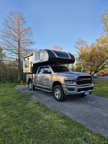 Graner rv rental: A grey Ram truck with a Palomino truck camper, parked on a paved spot amidst green grass & trees.