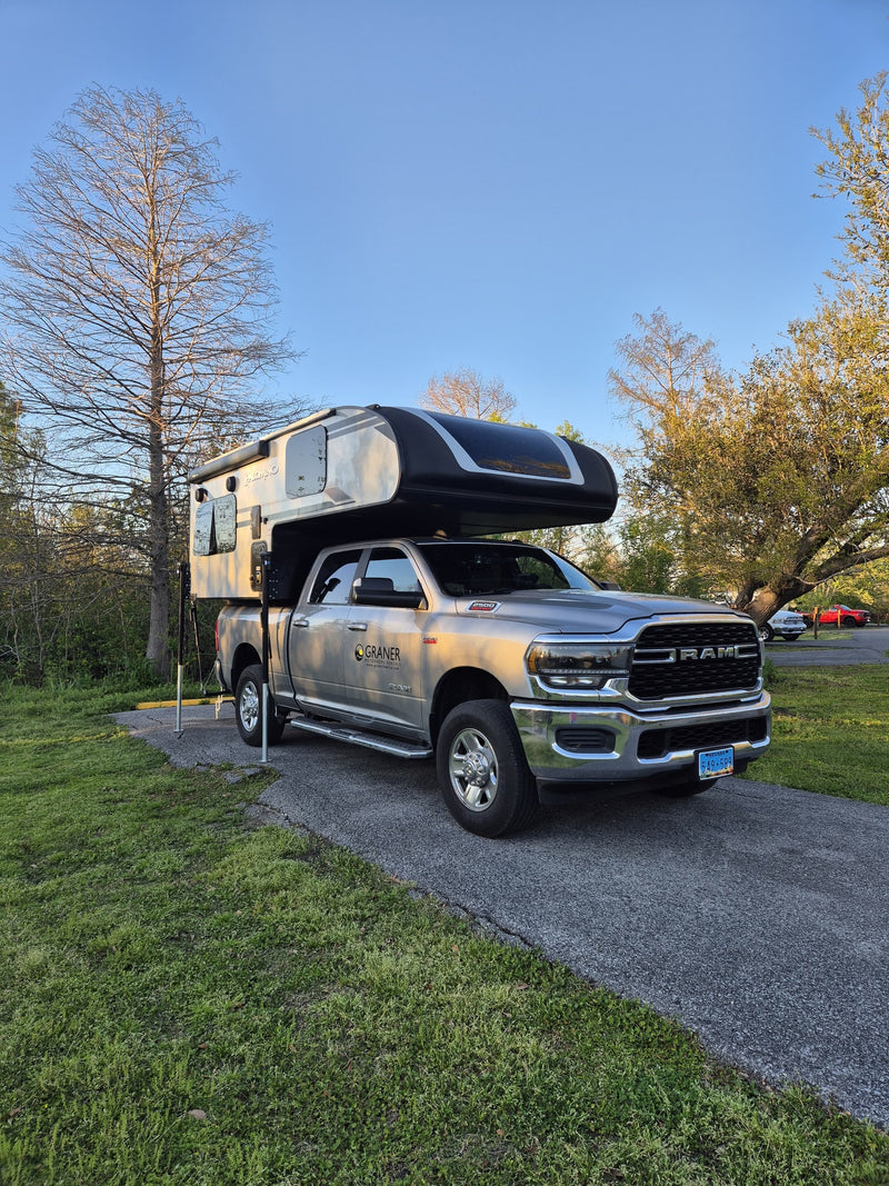 Graner rv rental: A grey Ram truck with a Palomino truck camper, parked on a paved spot amidst green grass & trees. — photo 9