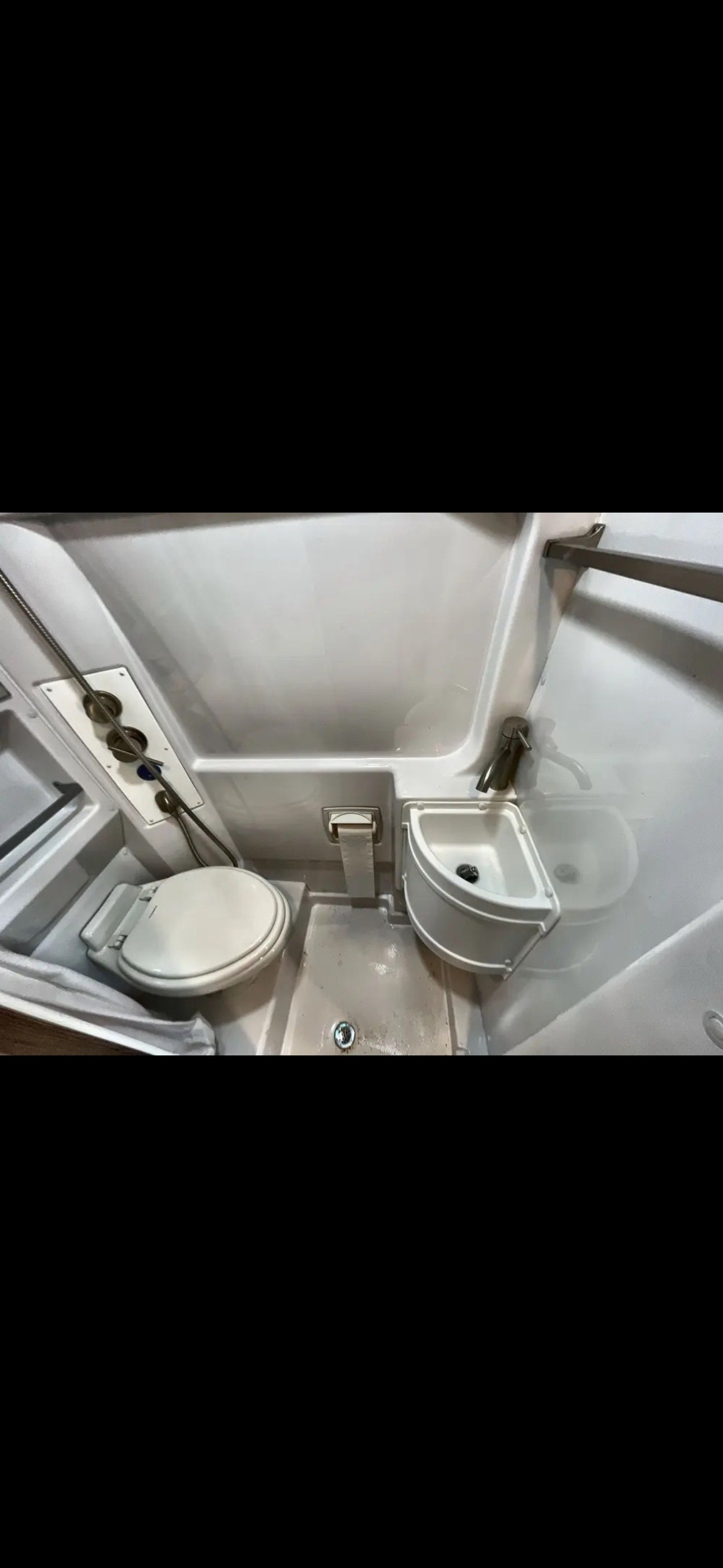 Inside an RV rental: a compact wet bath with toilet, small corner sink, and shower area, showing the floor drain. — photo 8