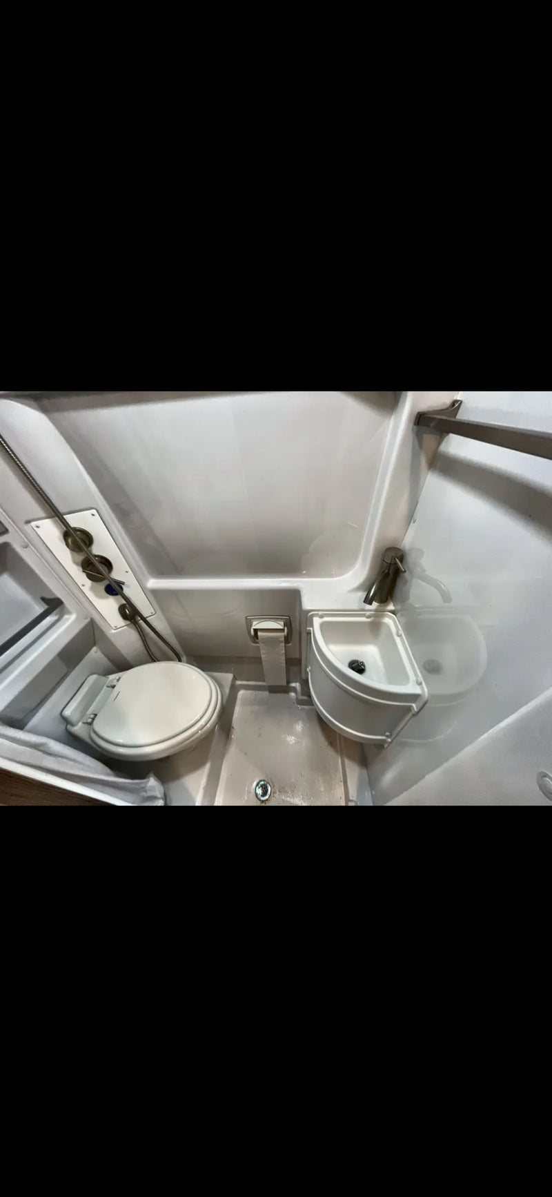 Inside an RV rental: a compact wet bath with toilet, small corner sink, and shower area, showing the floor drain. — photo 8
