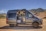 Modern gray camper van RV rental with open side door revealing interior, set against a backdrop of mountains and red rocks.