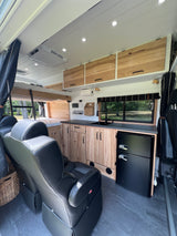 Modern RV rental interior: sleek kitchen, bunk bed, & leather captain's chairs. Brightly lit ceiling & scenic window views.