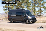 A dark gray camper van, ideal for RV rental adventures, parked on a dirt road with trees and mountains. Sale pending.