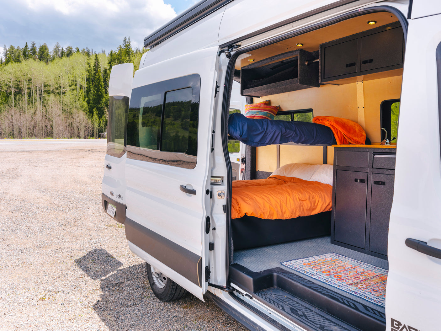 Open side of an RV rental van reveals a compact yet comfortable interior with bunk beds, kitchenette, and storage.