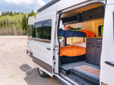 Open side of an RV rental van reveals a compact yet comfortable interior with bunk beds, kitchenette, and storage.