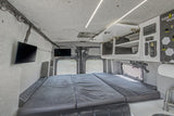 This spacious rv rental camper van interior features a comfy bed, dual TVs, kitchen area, and control panel for ultimate comfort.