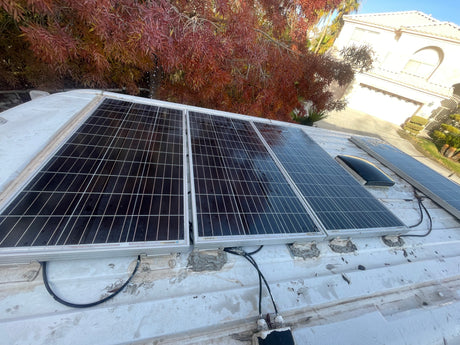 An RV rental's rooftop solar panels for off-grid adventures. View shows panels, wiring, sealant, and a house nearby.