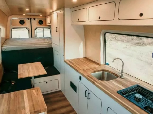  & wood finishes. Perfect for van life adventures.|This RV rental offers a compact dinette with a fold-down table and comfortable bench seating inside a camper van.|Explore this clean — photo 6