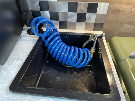 This **RV rental** features a practical utility sink with a flexible blue coiled sprayer hose for convenience.