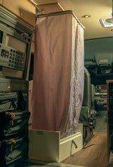 Inside an rv rental: a light pink shower curtain encloses a portable shower base, a clever space-saving van life feature.