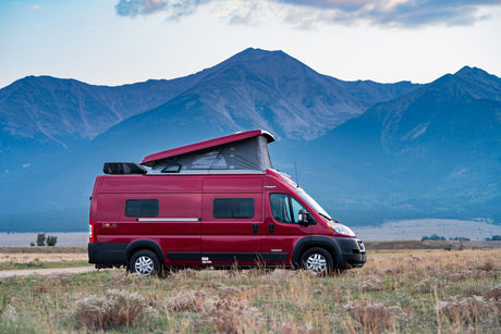 Red pop-top camper van (RV rental) in a scenic mountain setting, ideal for outdoor adventures and travel.