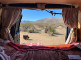 View from a cozy RV rental bed looking out at a serene desert landscape with mountains and cacti. Perfect for camping!