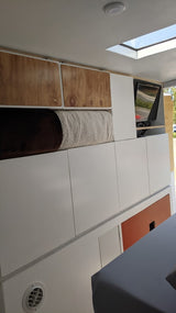 RV rental interior: cozy sleeping area with rolled blanket, white modular storage, wood overhead cabinets, TV, skylight.