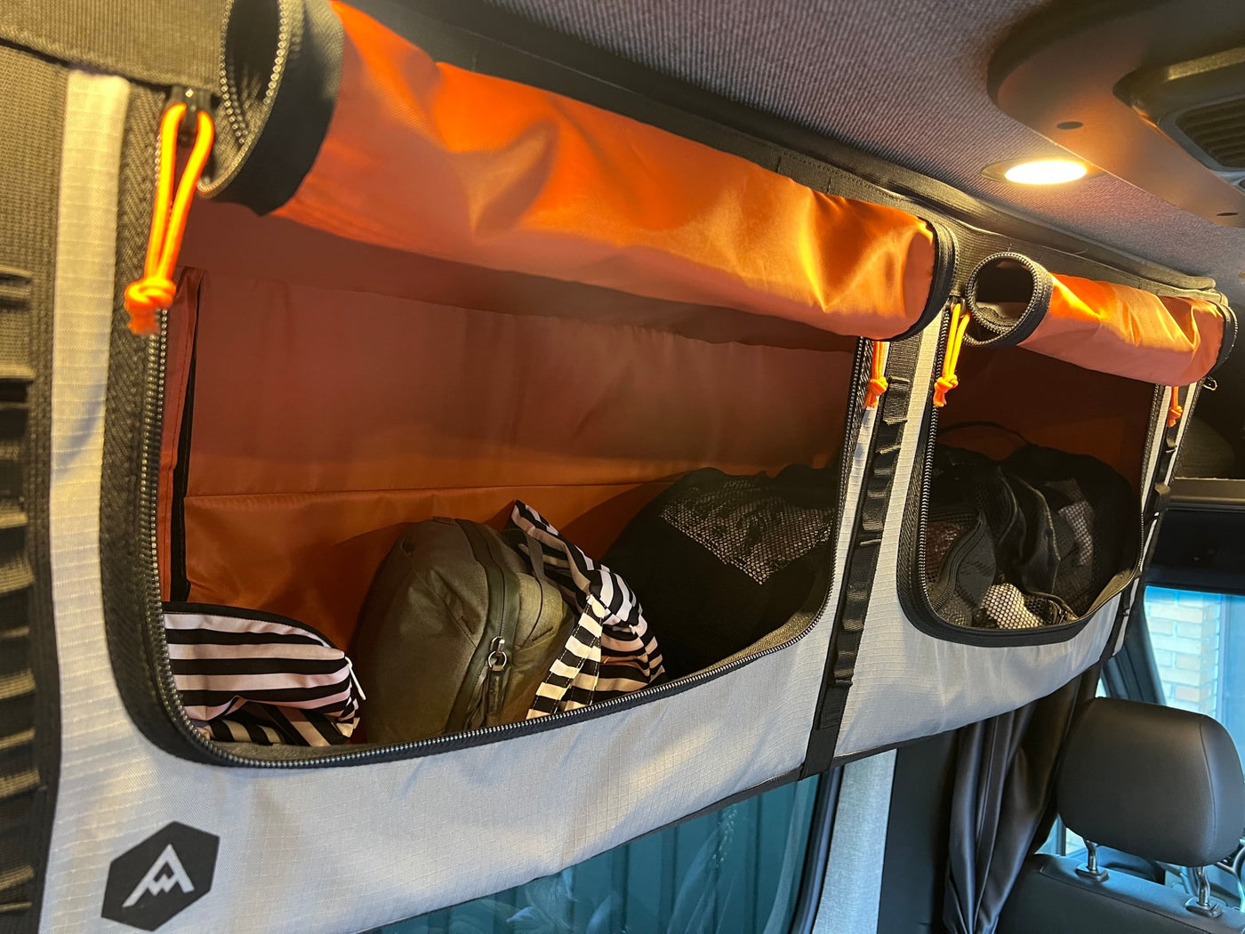 Efficient overhead storage in an rv rental with vibrant orange interiors, organizing gear like bags and clothing for easy access. — photo 13